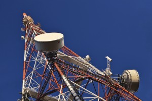 Telecommunication mast with microwave link and TV transmitter antennas over a blue sky.