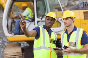 co-workers talking at construction site with bulldozer behind them